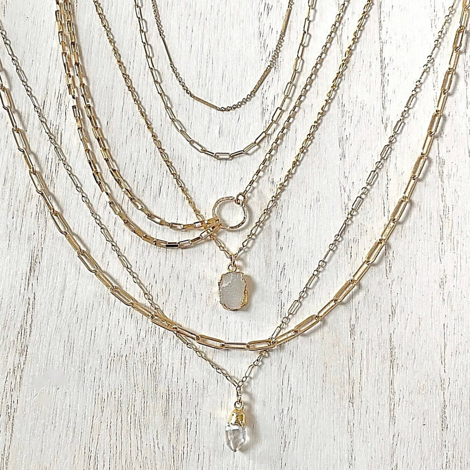 Stack of gold necklaces with various pendants on a light wooden surface