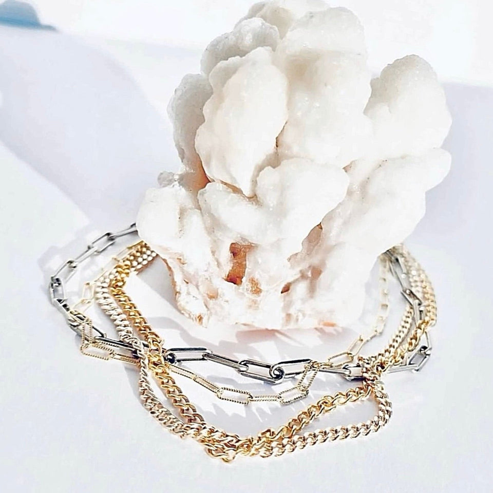 Gold and silver chain bracelets on a white surface with coral